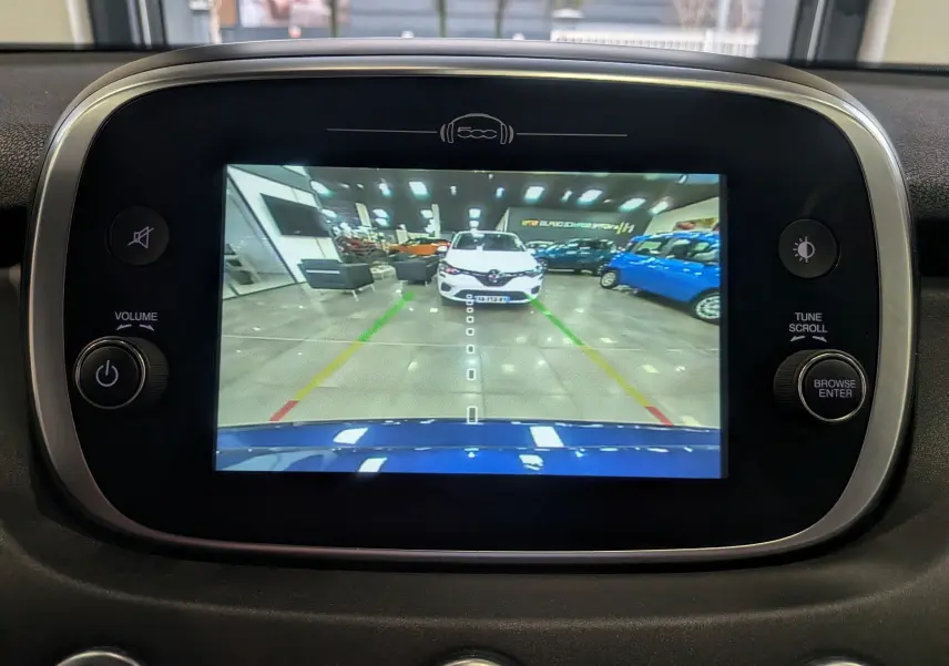 Vue caméra de recul sur écran intérieur du Fiat 500X bleu Venezia, montrant une voiture blanche en arrière-plan dans un showroom.