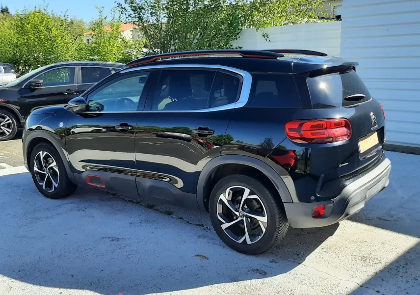 Vue 3/4 arrière droite d'un Citroën C5 Aircross noir avec jantes bicolores et détails rouges sur les protections latérales.