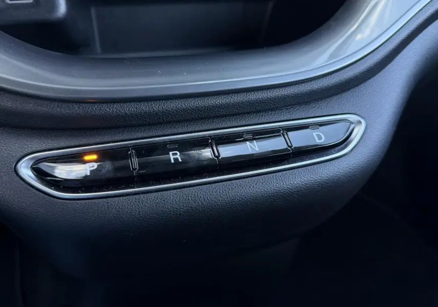 Gros plan sur la console centrale noire de la Fiat 500 électrique 2024 avec sélecteur de boîte auto et témoin de parking allumé.