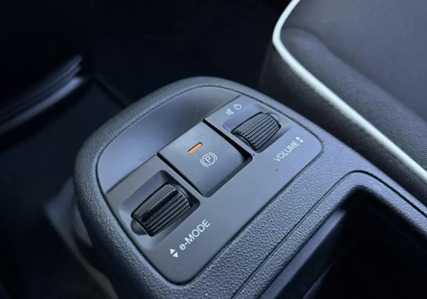 Gros plan sur la console centrale noire avec commandes e-Mode, frein à main électrique et réglage volume du Fiat 500 électrique blanc.