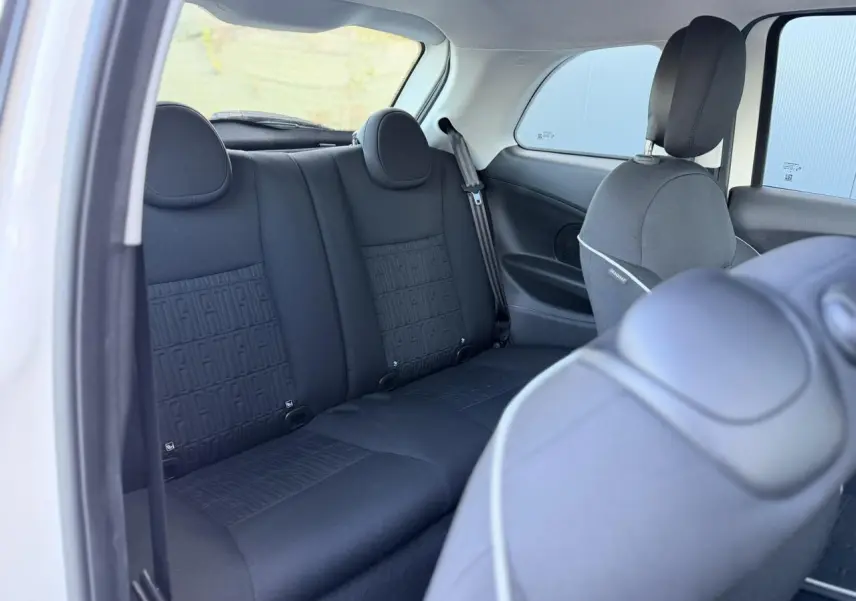 Vue intérieure arrière côté gauche montrant la banquette arrière noire avec motif FIAT sur la Fiat 500 électrique blanche.