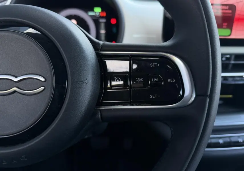 Gros plan sur le volant noir Soft-Touch de la Fiat 500 électrique, avec commandes de régulateur de vitesse visibles.