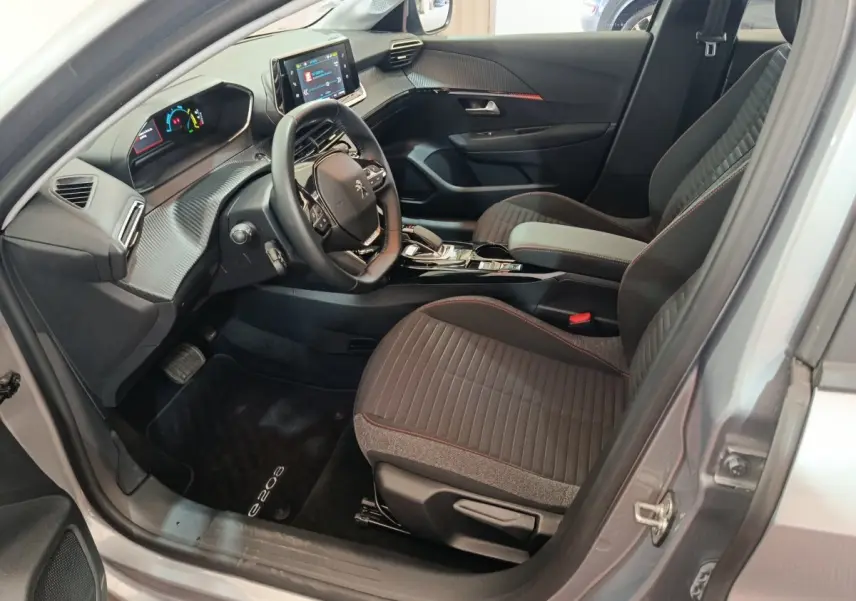 Intérieur avant droit de la Peugeot 208 électrique gris clair, avec tableau de bord digital et sièges tissu noir à surpiqûres rouges.