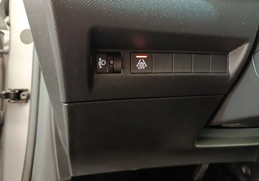 Gros plan sur les commandes de réglage des phares et désactivation de l'aide au maintien de voie dans une Peugeot 208 gris clair électrique.