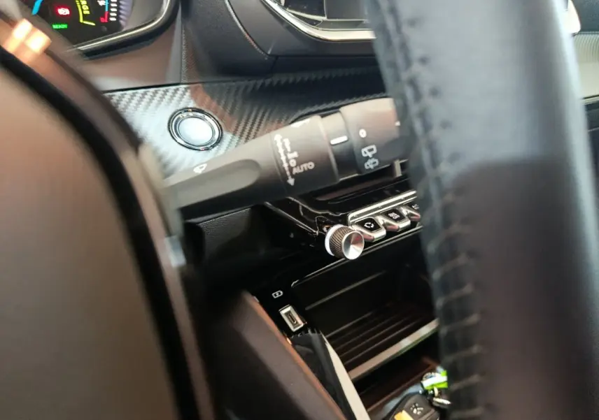 Détail intérieur côté conducteur du tableau de bord noir avec bouton démarrage et commandes Peugeot 208 électrique gris clair.