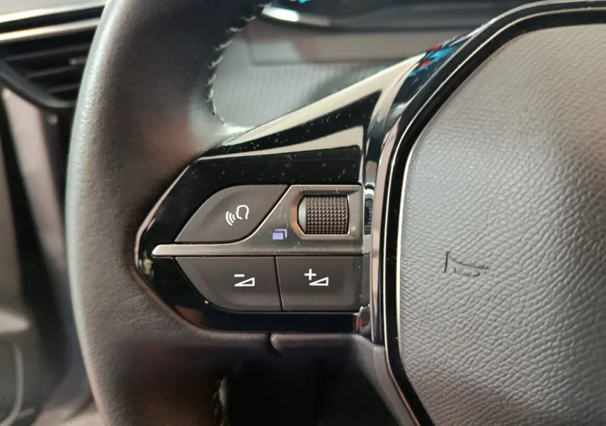 Gros plan sur les commandes du volant cuir noir du Peugeot 208 électrique Active Business gris clair, côté gauche.
