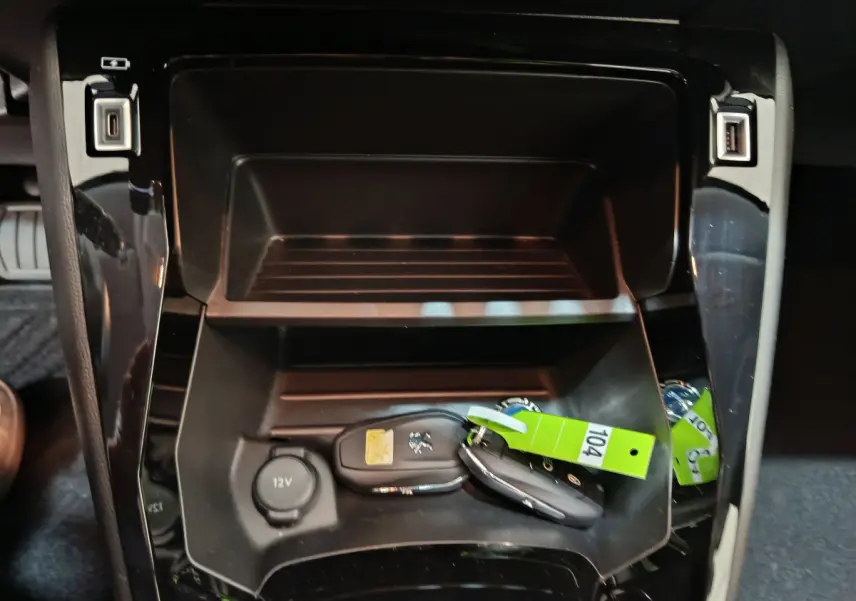 Rangement central noir avec clés Peugeot et prise 12V visible dans l'habitacle d'une 208 électrique gris clair.