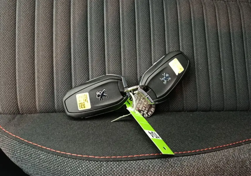Gros plan sur deux clés Peugeot posées sur un siège tissu gris foncé avec surpiqûres rouges.