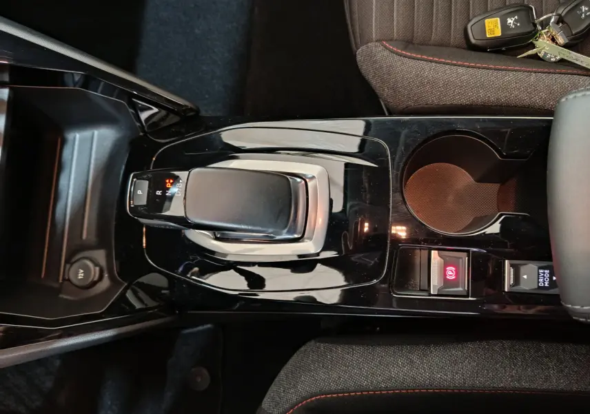 Vue rapprochée de la console centrale noire brillante avec levier de boîte auto et bouton frein à main électrique d’une Peugeot 208 Electrique Active Business.
