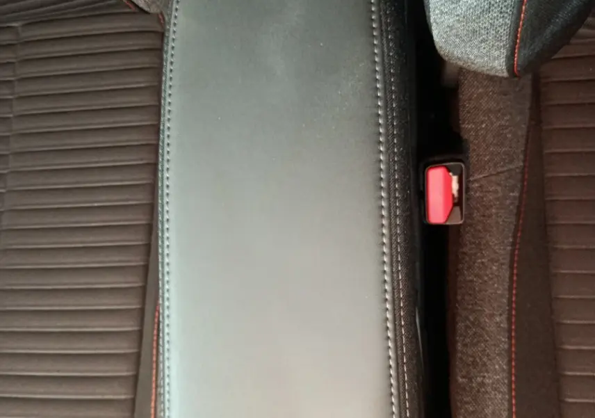 Vue plongeante sur l'accoudoir noir entre les sièges gris foncé avec surpiqûres rouges du Peugeot 208 Electrique Active Business.