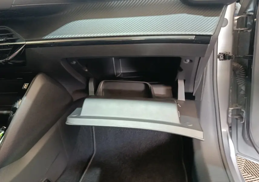 Vue intérieure côté passager de la Peugeot 208 électrique gris clair, montrant la boîte à gants ouverte et le tableau de bord.