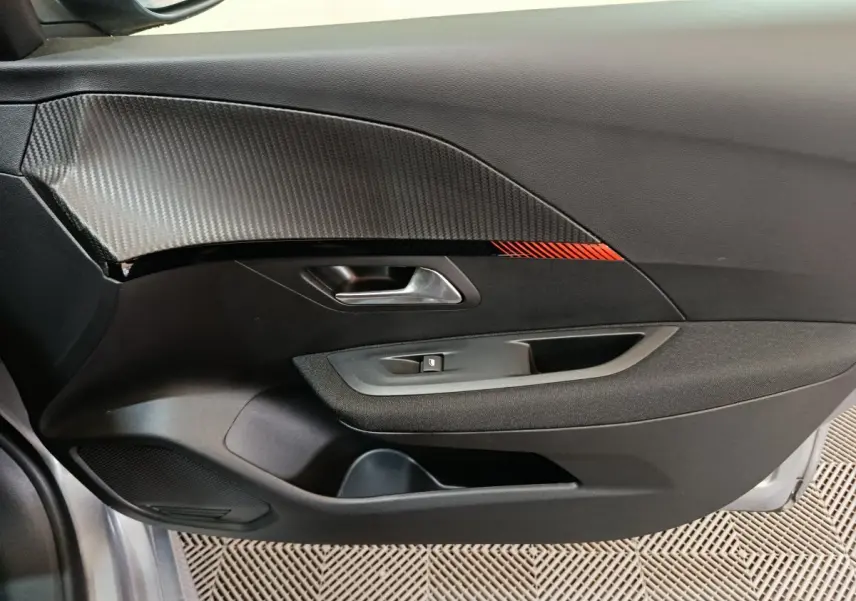Vue rapprochée de la porte côté gauche de la Peugeot 208 électrique gris clair avec insert carbone et détail rouge.