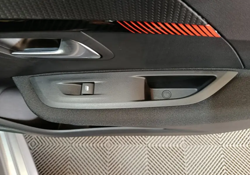 Poignée intérieure côté gauche avec bouton de lève-vitre sur la porte noire et décor rouge de la Peugeot 208 électrique 2020.