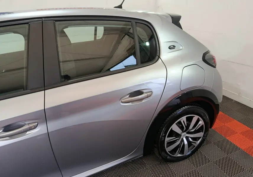 Vue côté droit arrière d'une Peugeot 208 électrique gris clair avec logo "e" distinctif près de la vitre arrière.