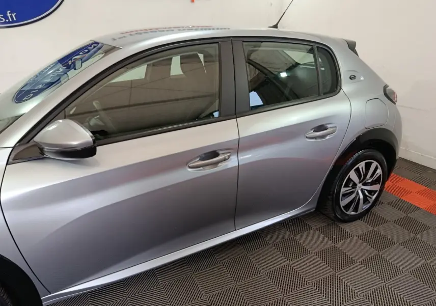 Profil côté gauche d'une Peugeot 208 électrique Active Business gris clair, avec jantes alliage et rétroviseur assorti.