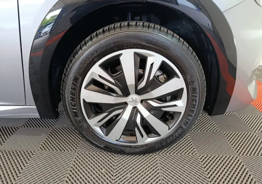 Gros plan sur la roue avant droite de la Peugeot 208 électrique gris clair avec jante alliage au design moderne.