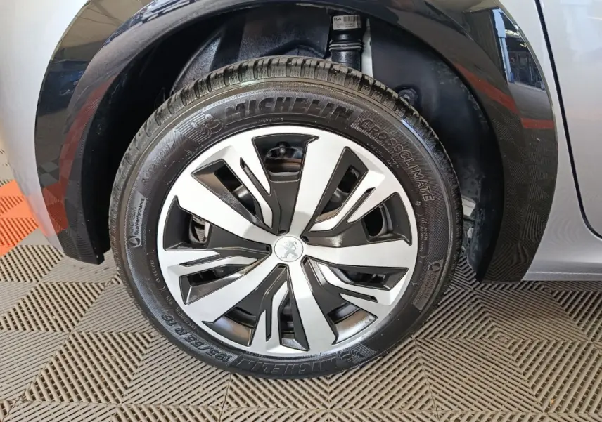 Gros plan sur la roue avant gauche gris clair d'une Peugeot 208 Electrique Active Business, jante moderne à motifs noirs et argentés.