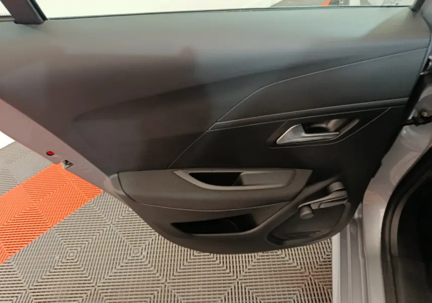 Vue intérieure de la porte arrière droite noire d'une Peugeot 208 électrique gris clair, avec poignée et haut-parleur intégrés.