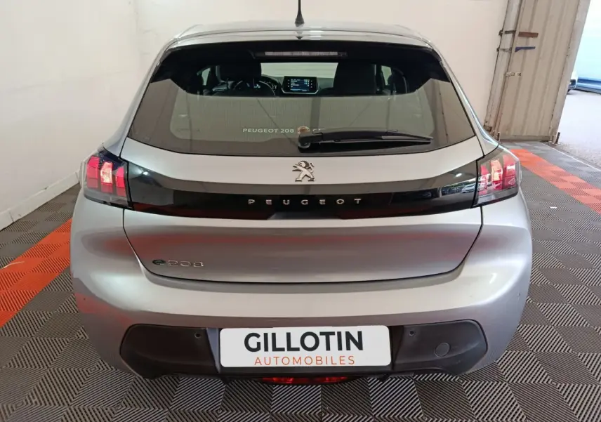 Vue arrière d'une Peugeot 208 électrique gris clair avec feux LED et logo lion sur hayon noir brillant.