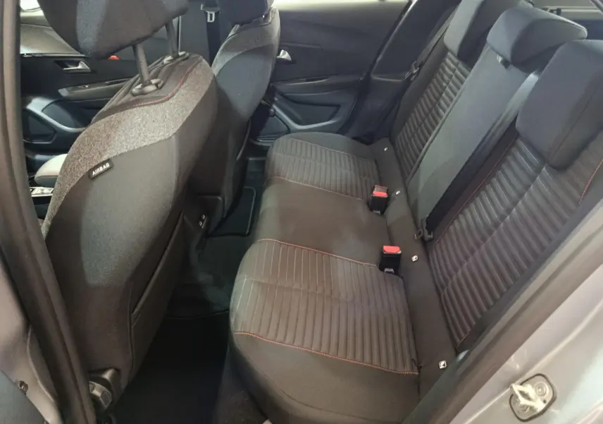Vue intérieure côté droit sur la banquette arrière noire avec surpiqûres rouges du Peugeot 208 Electrique gris clair.