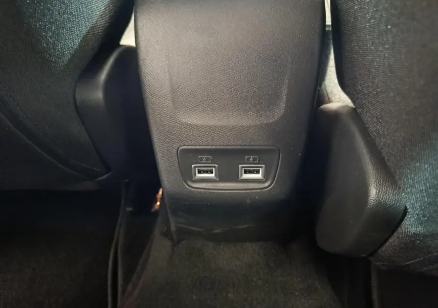 Prise double USB arrière au sol entre les sièges noirs de la Peugeot 208 électrique gris clair.