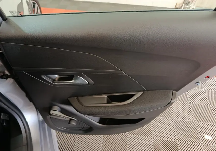 Intérieur côté gauche de la porte avant d'une Peugeot 208 électrique gris clair, avec poignée et commande de vitre manuelle.