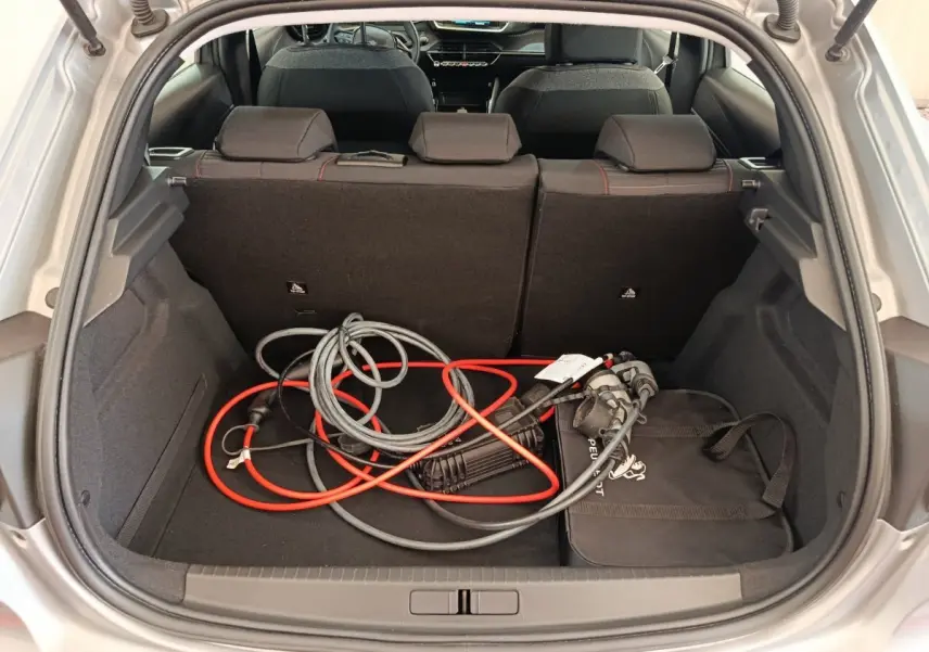 Coffre ouvert d'une Peugeot 208 électrique gris clair, montrant câbles de recharge et banquette arrière rabattable.
