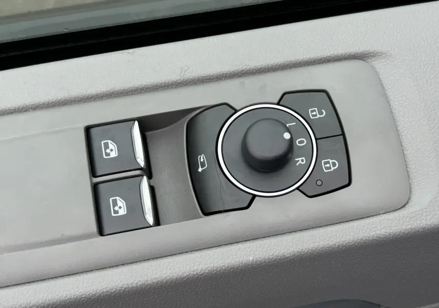 Gros plan sur les commandes de réglage des rétroviseurs et des vitres côté conducteur du Volkswagen Transporter T7 Business gris Graphite Dust.