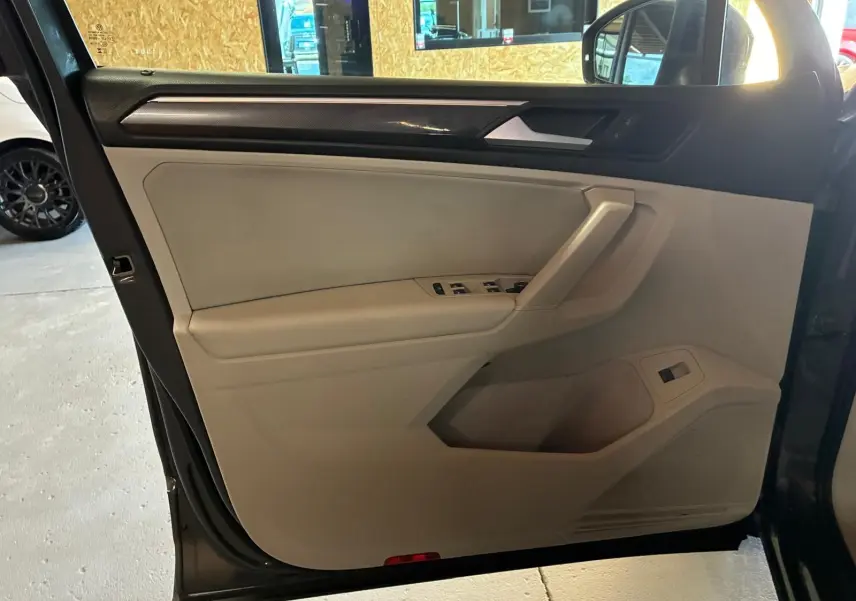 Vue intérieure côté gauche de la porte avant d’un Volkswagen Tiguan gris, avec commandes de vitres et garniture beige.