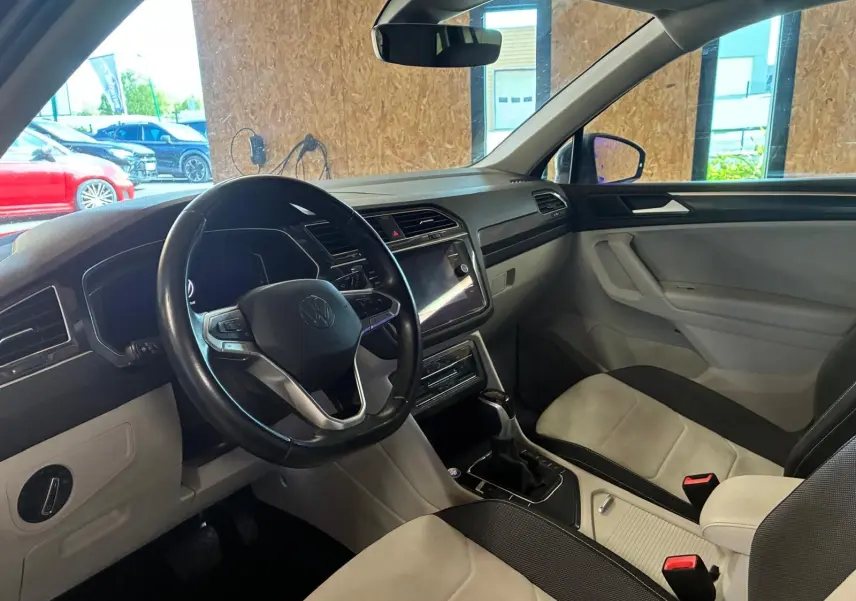 Vue intérieure côté conducteur du Volkswagen Tiguan 2023, volant cuir multifonctions et sièges tissu clair et noir.