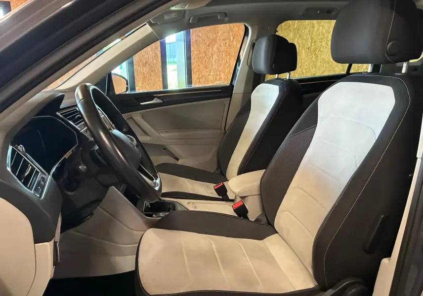Vue intérieure côté conducteur du Volkswagen Tiguan 2023, sièges bicolores gris clair et noir avec volant cuir.