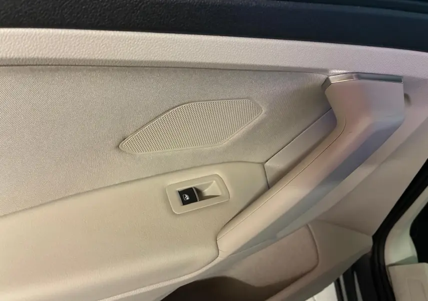 Gros plan sur la poignée intérieure côté gauche du Volkswagen Tiguan gris, avec bouton de commande de vitre électrique.
