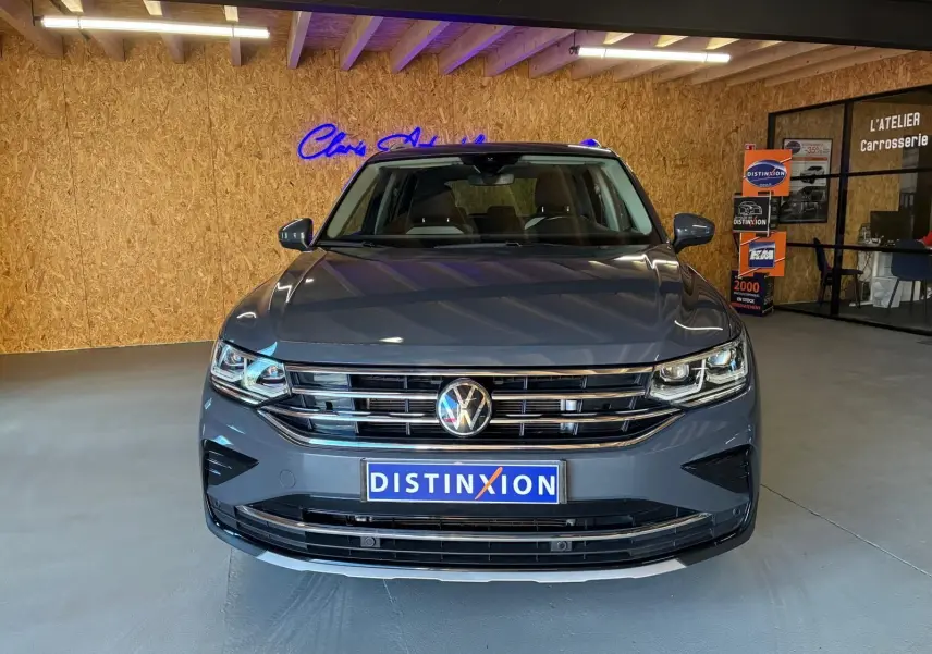 Vue avant d'un Volkswagen Tiguan gris 2023 avec calandre chromée et plaque Distinxion en intérieur showroom.