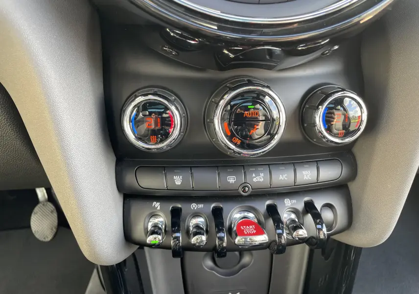 Gros plan sur la console centrale de la MINI F56 Cooper S 2015, montrant les commandes de climatisation et le bouton start/stop rouge.