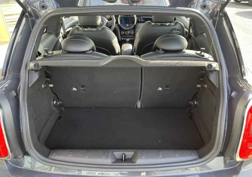 Coffre ouvert vu de l'arrière d'une MINI F56 Cooper S gris Thundergrey, intérieur noir avec sièges et tableau de bord visibles.