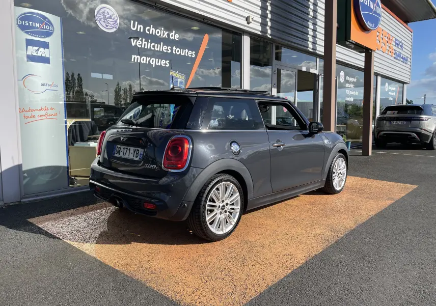Vue 3/4 arrière droite d'une MINI F56 Cooper S gris Thundergrey avec jantes 17 pouces et toit noir devant un showroom.