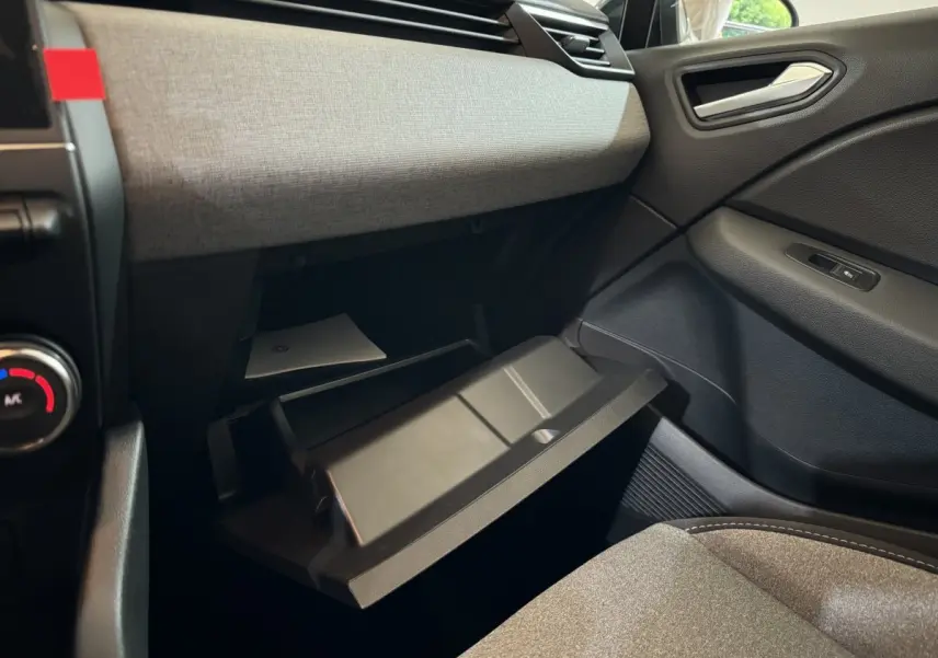 Intérieur de la Renault Clio 2025 gris clair, vue côté passager avec boîte à gants ouverte et tissu clair sur planche de bord.