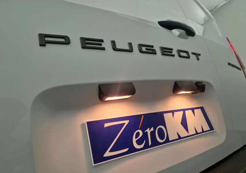 Gros plan sur l'arrière blanc du Peugeot Partner 2025 avec éclairage plaque et logo noir visible.