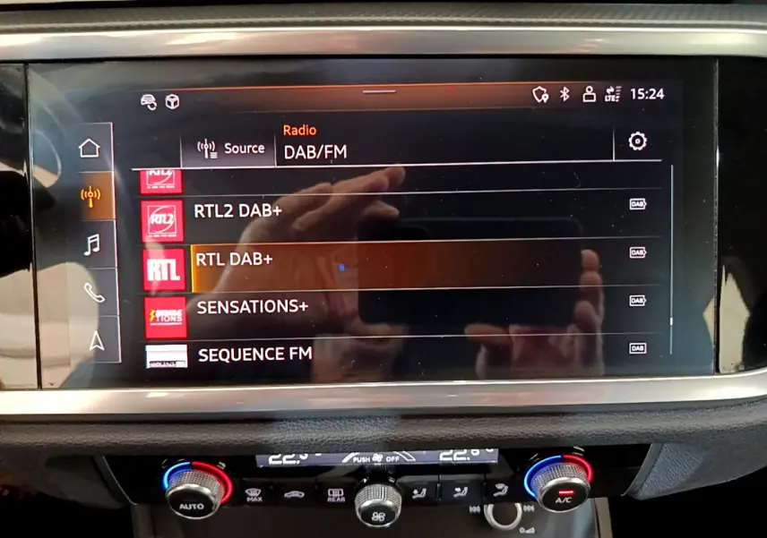 Écran tactile central affichant les stations radio DAB/FM dans l'habitacle d'un Audi Q3 noir, vue de face rapprochée.