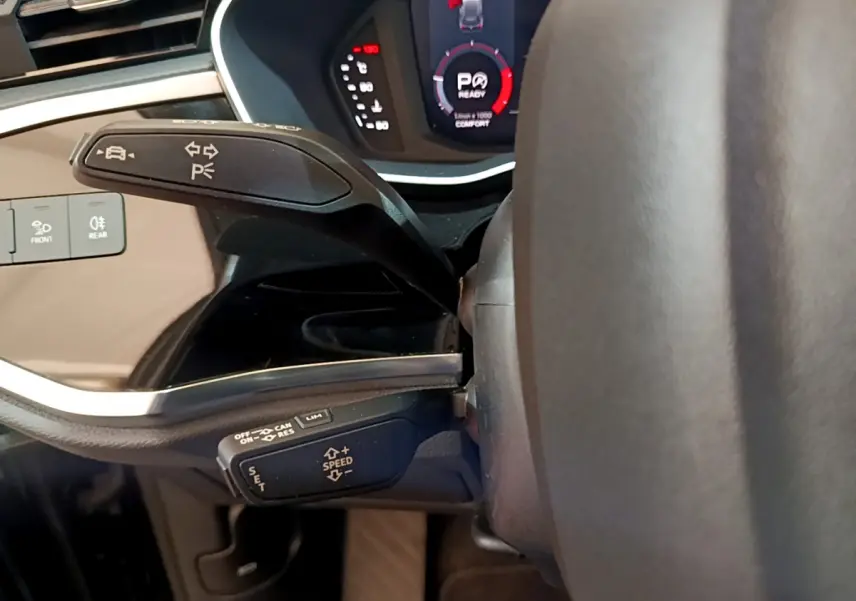 Vue rapprochée du levier de commande multifonctions côté gauche du volant d’un Audi Q3 noir, tableau de bord digital visible.