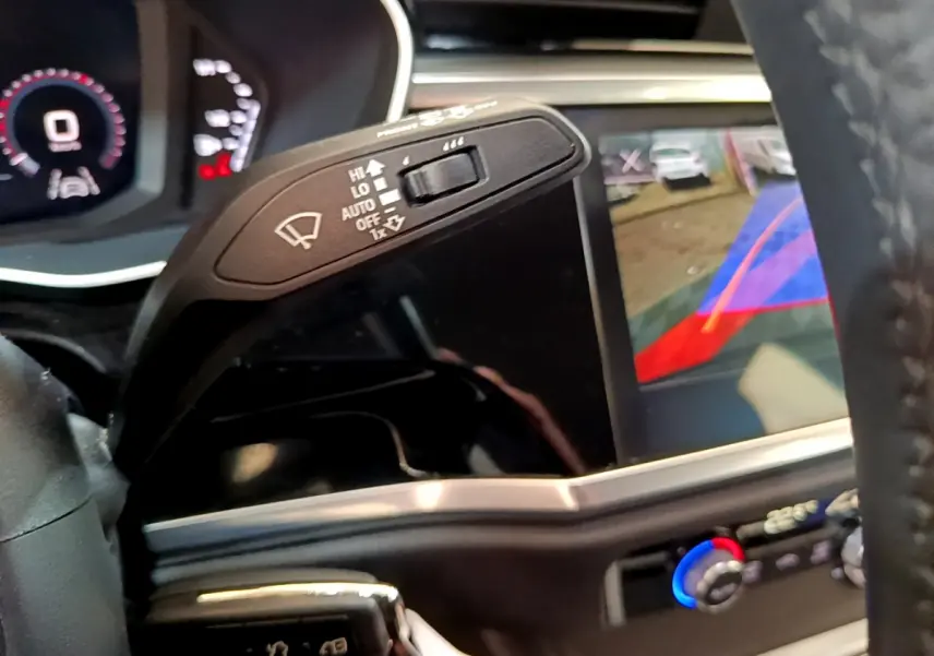 Gros plan intérieur sur le commodo d’essuie-glace et l’écran tactile avec caméra de recul de l’Audi Q3 noir, vue côté conducteur.