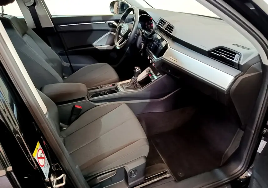 Intérieur avant droit de l’Audi Q3 noir 2021, montrant sièges tissu, tableau de bord moderne et volant multifonctions cuir.