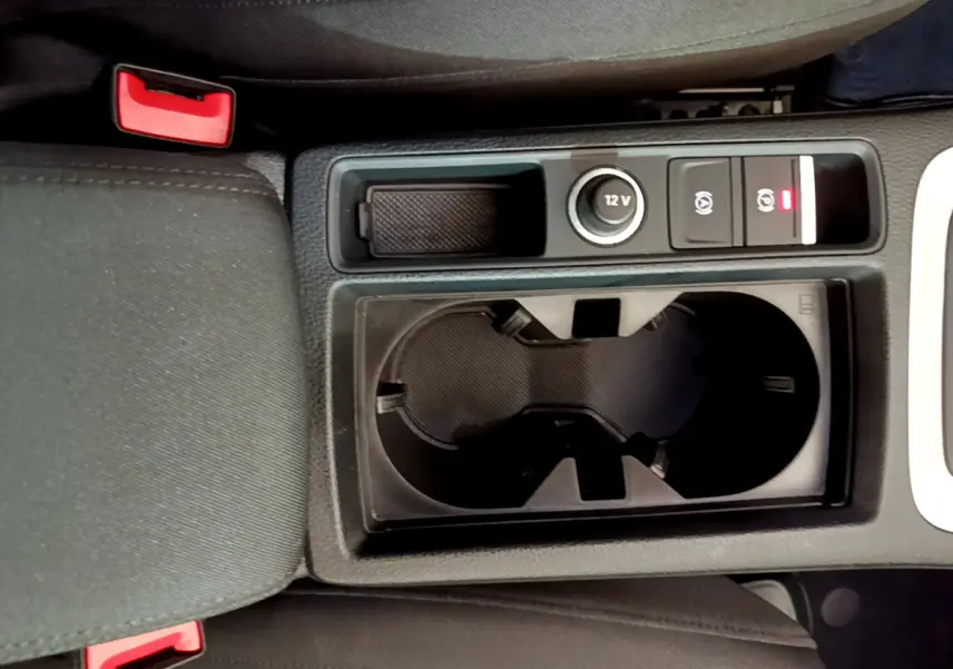 Vue plongeante sur la console centrale noire de l'Audi Q3 35 TDI 150 S tronic avec porte-gobelets et bouton 12V.