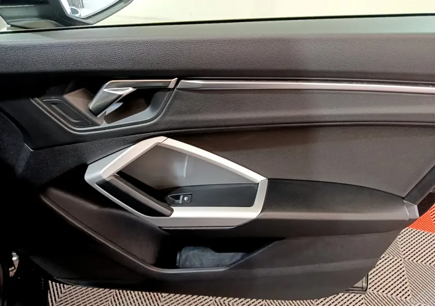 Vue intérieure du panneau de porte avant gauche noir avec poignée argentée et commande de lève-vitre Audi Q3 2021.