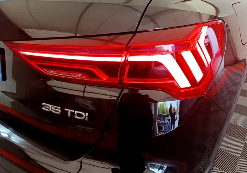 Gros plan sur le feu arrière droit rouge allumé d’un Audi Q3 noir 35 TDI avec logo visible sur le coffre.