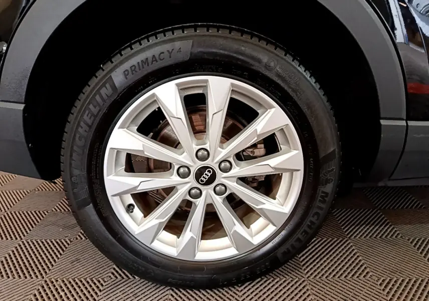Gros plan sur la roue avant droite d’un Audi Q3 noir, mettant en valeur la jante alliage argentée et le pneu Michelin.