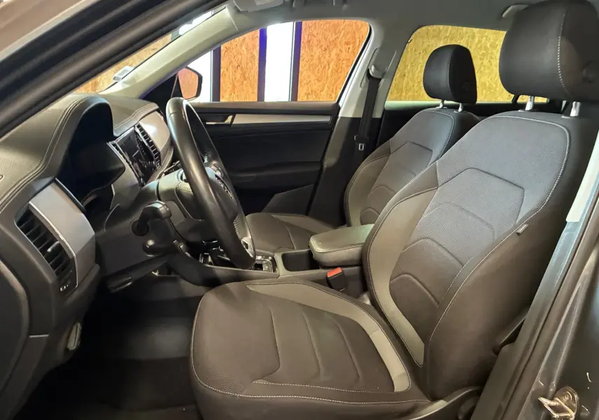 Vue intérieure côté conducteur du Skoda Kodiaq 2023, sièges tissu gris et tableau de bord avec volant cuir.