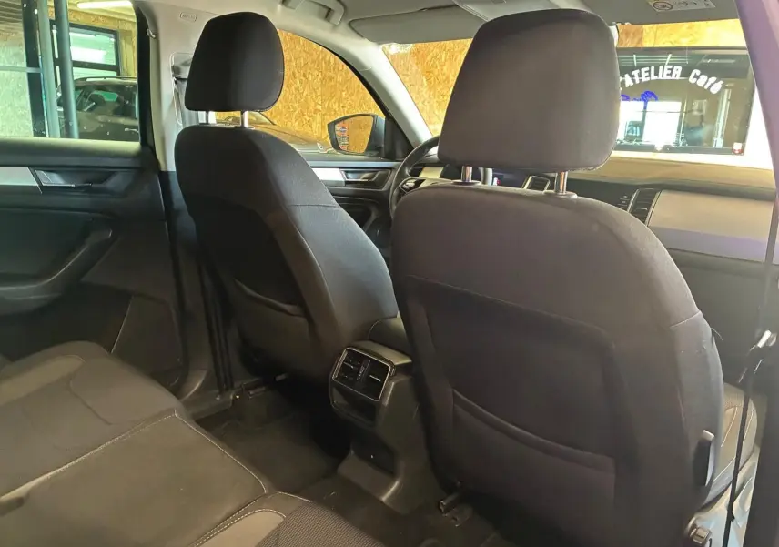 Vue intérieure arrière du Skoda Kodiaq gris 7 places, montrant les sièges avant en tissu noir et la console centrale avec aérateurs.