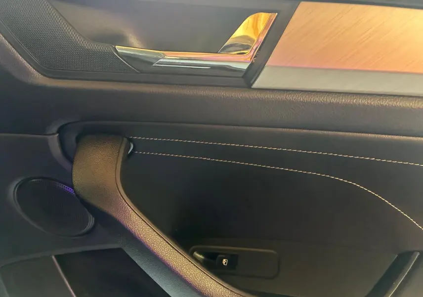Détail de la porte intérieure côté gauche d’un Skoda Kodiaq gris, avec insert bois et surpiqûres blanches.