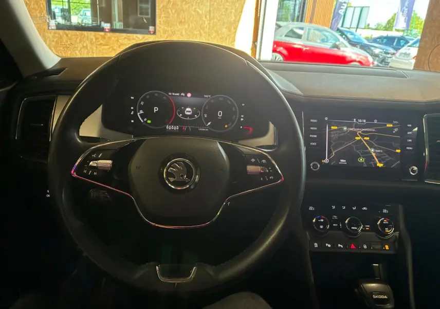 Vue intérieure centrée sur le volant noir et le tableau de bord digital du Skoda Kodiaq 2023 avec écran GPS allumé.